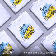 Футболка все буде Україна, біла, зображена з правого ракурсу на манекені, фон світло-сірий, принт з написом 'Все буде Україна' у жовто-блакитних кольорах.