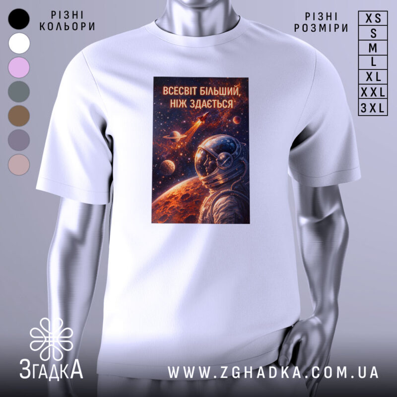 Футболка всесвіт більший, біла, зображена з правого ракурсу, на фоні світло-сірого градієнту, принт з космічним астронавтом та планетами, яскраві кольори принта на темному фоні.
