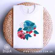 Футболка вишневі гілки, біла, складена на плетеному кошику, фон світлий, принт з червоними вишнями та зеленим листям на кольорових фонах.