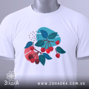 Футболка вишневі гілки, біла, складена на столі, фон світлий, принт з червоними вишнями та зеленим листям, з етикеткою на шнурку.