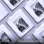 Футболка висота не велич. Біла футболка з чорним принтом, на якому зображений чоловік, що дивиться на будівлю на вершині пагорба. Фон з легкими горизонтальними лініями, що імітують небо. Принт детально передає текстуру одягу персонажа.