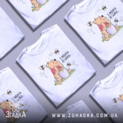 Футболка з любовʼю до бджіл, білого кольору, зображена на манекені, фон нейтральний, принт з ведмедиком, що тримає банку з медом, оточений бджолами.