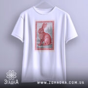 Футболка заєць лісовий, біла, підвішена на вішалці, фон світло-сірий, принт з червоним зайцем в рамці, видно деталі рукавів.