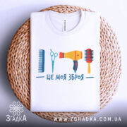 Футболка зброя перукаря, біла, зображена зверху на плетеній основі, фон білий, принт містить гребінець, ножиці, фен та щітку, яскраві кольори.