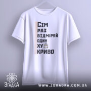 Футболка жарт про майстрів, біла, зображена з фронтального ракурсу, фон світлий, принт містить текст "Сім раз відміряй один хукриво" та малюнок персонажа, лінійка розташована зліва.