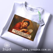 Футболка жартівлива гадалка, біла, зображена на столі, фон світло-сірий, принт з жінкою в червоному шарфі, яка тримає карти, текст на принті чорний, прикріплена етикетка з зеленим шнурком.