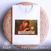 Футболка жартівлива гадалка, біла, зображена на столі, фон плетений, принт з жінкою в червоному шарфі, яка тримає карти, текст на принті чорний, розташований під зображенням.