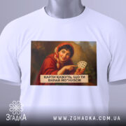 Футболка жартівлива гадалка, біла, зображена на столі, фон світло-сірий, принт з жінкою в червоному шарфі, яка тримає карти, текст на принті чорний, прикріплена етикетка з зеленим шнурком.