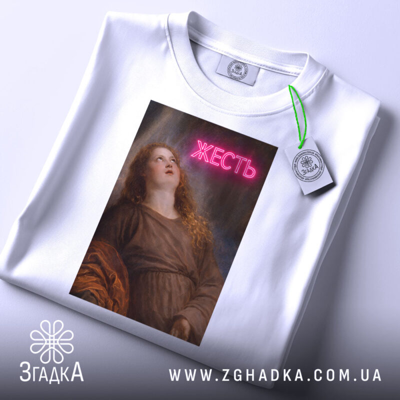 Футболка жесть класика, біла, складена на поверхні, фон світло-сірий, принт з дівчиною, яка дивиться вгору, з написом 'ЖЕСТЬ' у неоновому стилі, на футболці є етикетка з зеленим шнурком.