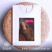 Футболка жесть класика, біла, складена на кошику, фон світло-сірий, принт з дівчиною, яка дивиться вгору, з написом 'ЖЕСТЬ' у неоновому стилі.
