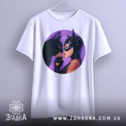 Футболка жінка котик, біла футболка, підвішена на вішалці, з круглим принтом, на якому зображена жінка в масці, що торкається носа чорного кота, фон фіолетовий, ракурс спереду.