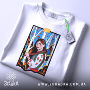 Футболка жіноча відвага, біла, зображена зверху, фон світло-сірий, принт з дівчиною в українському вбранні, що тримає сокиру, на фоні дерев з червоними листям, з етикеткою на комірці.