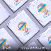 Футболка жіночий образ України, біла, зображена з фронтального ракурсу, фон світло-сірий, принт з малюнком дівчини з косою та кольоровими смугами синього і жовтого кольору, текст 'Ukraine' під малюнком.