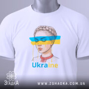 Футболка жіночий образ України, біла, зображена зверху, фон світло-сірий, принт з малюнком дівчини з косою, кольорові смуги синього і жовтого кольору, текст 'Ukraine' під малюнком, на футболці є етикетка з зеленим шнурком.