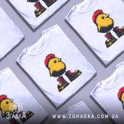 Футболка Жовта пташка, біла футболка на манекені, з принтом жовтої пташки в червоних черевиках, фон світло-сірий, пташка має чорний гребінь і деталі на грудях.