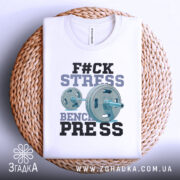 Футболка жим замість стресу, біла, складена на плетеній кошику, фон світлий, принт з написом 'F#CK STRESS' та зображенням гантелі, виконаний у блакитних та чорних кольорах.