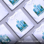 Футболка Житомир, біла, зображена на манекені, фон градієнтний сірий, принт з зображенням будівлі з годинником та українським прапором, кольори принта: блакитний, зелений, помаранчевий.