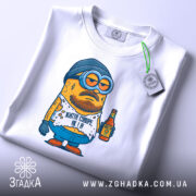 Футболка життя суворе, біла, складена на столі, фон світлий, принт з мультяшним персонажем у шапці та окулярах, тримає пляшку, текст на футболці: 'Життя суворе, як я!', з етикеткою на рукаві.