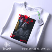 Футболка живи життя, біла, зображена зверху, на фоні світло-сірого градієнту, принт з зображенням кролика в светрі з гербом України, з димом та сигаретою, текст "ЖИВИ ЖИТТЯ" червоним кольором, з зеленим ярликом.