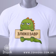 Футболка злюкозавр сердитий, біла, зображена зверху, фон світло-сірий, принт злюкозавра з зеленим тілом, тримає табличку з написом 'ЗЛЮКОЗАВР', на футболці є етикетка з зеленим шнурком.