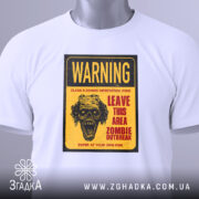 Футболка зомбі попередження, біла, складена на поверхні, фон світлий, принт з черепом та текстом жовтого кольору, з етикеткою.