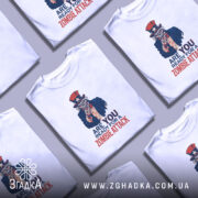 Футболка zombie attack білого кольору, зображена на манекені з правого боку, фон світло-сірий, принт з черепом у капелюсі зірки та написом 'ARE YOU READY FOR A ZOMBIE ATTACK' у червоному та синьому кольорах.