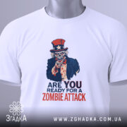 Футболка zombie attack білого кольору, складена на поверхні, фон світло-сірий, принт з черепом у капелюсі зірки та написом 'ARE YOU READY FOR A ZOMBIE ATTACK' у червоному та синьому кольорах, з етикеткою на рукаві.