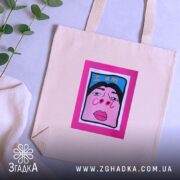 Шопер для класних бежевий, з ракурсом зверху, на фоні світлого столу з рослинами, з тонкої бавовняної тканини, довжина ручок середня, місткість достатня для повсякденних речей, принт з написом 'I am cool' на яскравому рожевому фоні.