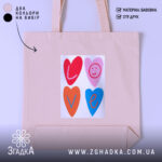 Шопер для закоханих. Бежевий, зображення спереду, на світлому фоні. Тканина середньої товщини, ручки середньої довжини, місткість достатня для повсякденних речей, принт з серцями та написом 'LOVE' у яскравих кольорах.