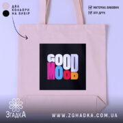 Шопер Good Mood, бежевого кольору, зображений з близької відстані на світлому фоні, з товстої бавовняної тканини, ручки середньої довжини, місткий, з принтом на чорному фоні з написом 'GOOD MOOD' різнокольоровими літерами.