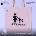 Шопер яжмама, бежевий, з фронтальної сторони, на світлому фоні, тонка бавовняна тканина, ручки середньої довжини, місткий, принт з жінкою в сукні та двома дітьми, напис #ЯЖМама!