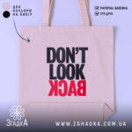 Шопер не дивись назад. Бежевий колір, фронтальний ракурс, фон світлий. Тканина середньої товщини, ручки середньої довжини. Місткість достатня для повсякденних речей, принт з написом 'DON'T LOOK BACK' в чорному та червоному кольорах.