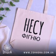 Шопер несу фігню, бежевий, зображений зверху на фоні текстури, великий чорний напис 'НЕСУ ФІГНЮ', з двома ручками, прямокутна форма, місткість підходить для повсякденних речей.