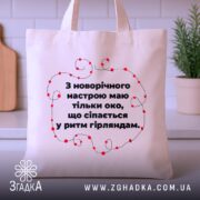 Шопер святковий настрій, бежевий, з фронтальної сторони, на фоні кухонних приладів, з тонкої бавовняної тканини, ручки середньої довжини, місткий, з принтом у вигляді червоних гірлянд навколо тексту.