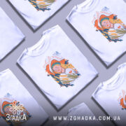 Футболка Українська дівчина білого кольору, зображена на манекені, ракурс спереду, фон світло-сірий, принт з дівчиною з довгим волоссям, що тримає колосся, оточена кольоровими елементами.