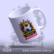 Чашка для короля футболу, біла, зображена з легким нахилом, фон світло-фіолетовий, принт містить футбольний м'яч, корону та напис "КОРОЛЬ своєї гри МАКСИМ", ручка класична, край рівний, глянець.