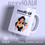 Чашка для щасливої Юлі. Чашка білого кольору з глянцевим покриттям, зображення дівчини з коктейлем на передній стороні. Ручка круглої форми, край чашки рівний. Фон ніжно-фіолетовий, текст чорного кольору з веселим шрифтом.