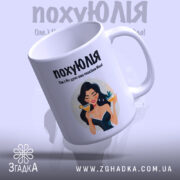 Чашка для щасливої Юлі. Біла чашка з глянцевим покриттям, зображення дівчини з коктейлем на передній стороні, що злегка нахилена. Ручка круглої форми, край чашки рівний. Фон ніжно-фіолетовий, текст чорного кольору.