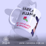 Чашка для справжньої відьми, біла з малюнком відьми, ракурс зліва, фон світло-фіолетовий, принт містить напис "ЧАШКА ВІДЬМИ" та малюнок з келихом, ручка кругла, край рівний, матова поверхня.