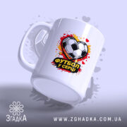 Чашка Футбол у серці, біла, з зображенням футбольного м'яча у формі серця, ручка стандартна, край рівний, фон з розмитими плямами червоного і жовтого кольору, глянцева поверхня.