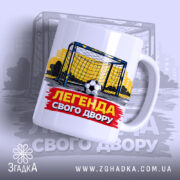 Чашка футбольна Легенда двору, біла, зображення футбольних воріт на жовтому фоні, напис 'ЛЕГЕНДА СВОГО ДВОРУ' червоного кольору, ручка кругла, край рівний, матова поверхня.