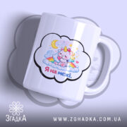 Чашка Я на межі. Біла чашка з малюнком єдинорога, який спить на хмарах, з веселкою та зірками. Ручка чашки гладка, край рівний, поверхня глянцева. Фон ніжно-фіолетовий.