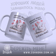 Чашка хороших людей мало. Дві чашки білого кольору, одна з них повернута до камери, з малюнком кролика та сердечками. Ручки чашок гладкі, краї рівні, поверхня глянцева. На чашках напис: 'Бережіть мене!'