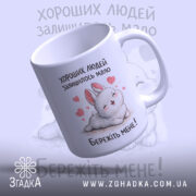 Чашка хороших людей мало. Чашка білого кольору, зображена з легким нахилом, з малюнком кролика та сердечками. Ручка гладка, край рівний, поверхня глянцева. На чашці напис: 'Бережіть мене!'