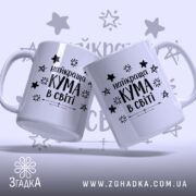 Чашка найкращої куми двох білих чашок, що стоять під кутом одна до одної, з чорним написом "найкраща КУМА в світі" та зірочками на фоні, ручки гладкі, краї рівні, поверхня глянцева.