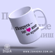 Чашка про дружбу подрузі, біла, з ракурсом з правого боку, на фоні світло-фіолетового кольору, з чорним написом "Подруга – це ❤️ яке не купиш", ручка круглої форми, край рівний, глянцева поверхня.