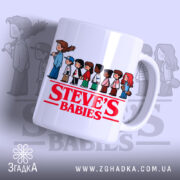 Чашка Steve's Babies має білий фон з яскравим червоним написом 'STEVE'S BABIES' на передній частині, з малюнками дітей, що стоять в ряд. Ручка чашки гладка, край рівний, а поверхня має легкий глянець.