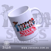 Чашка Steve's Babies з білим фоном, на якому розташовані малюнки дітей та червоний напис 'STEVE'S BABIES'. Ручка чашки гладка, край рівний, а поверхня має легкий глянець, що підкреслює яскравість принта.