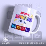 Чашка Ти ж Дизайнер. Чашка білого кольору з яскравим принтом, на якому написано 'ЗРОБИ КРАСИВО ТИ Ж' у різних кольорах. Ручка класичної форми, край рівний, поверхня глянцева. Фон світло-фіолетовий з розмитими елементами.