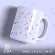 Чашка з кольоровими піструнами, біла з яскравими малюнками у формі кісточок різних кольорів, зображена під кутом, фон світло-фіолетовий, ручка стандартна, край рівний, глянцева поверхня.